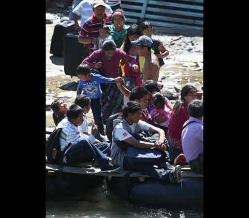 Grupo de inmigrantes indocumentados cruzan la frontera a bordo de una balsa improvisada, que navega justo debajo de un puente en donde se ubica un retén de la agencia aduanal mexicana.