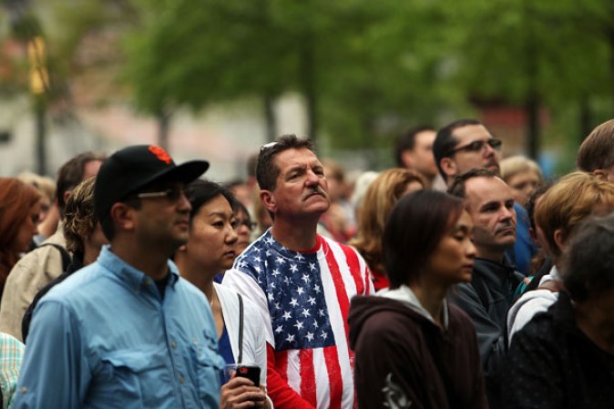 NEW YORK, NY - MAY 15: People watch a live video from the Ground Zero memorial site of the dedication ceremony of the National September 11 Memorial Museum in New York May 15, 2014 in New York City. The museum spans seven stories, mostly underground, and contains artifacts from the attack on the World Trade Center Towers on September 11, 2001 that include the 80 ft high tridents, the so-called "Ground Zero Cross," the destroyed remains of Company 21's New York Fire Department Engine as well as smaller items such as letter that fell from a hijacked plane and posters of missing loved ones projected onto the wall of the museum. The museum will open to the public on May 21. (Photo by Spencer Platt/Getty Images)