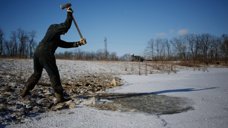 Este campesino en Louisville, Kansas rompe el hielo de un pozo congelado para que sus animales puedan beber agua.