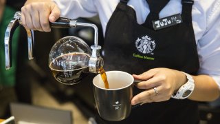 An employee pours coffee from a round glass jug into a mug at a Starbucks