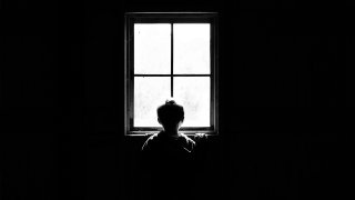 Stock photo of a silhouetted child standing at window in dark room.