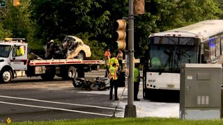 A totaled sedan sits on the bed of a tow truck as the NJ Transit bus with wich it collided rests near the sidewalk in Moorestown, New Jersey.