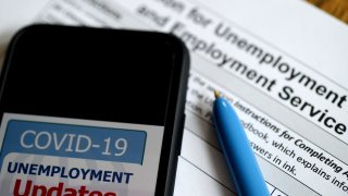 In this photo illustration, a COVID-19 Unemployment Assistance Updates logo is displayed on a smartphone on top of an application for unemployment benefits on May 8, 2020, in Arlington, Virginia.