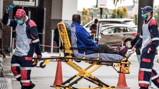 In this July 10, 2020, file photo, an emergency paramedic wearing full COVID-19 coronavirus personal protective equipment (PPE) flashes the victory sign as they arrive with a patient at the Greenacres Hospital in Port Elizabeth.