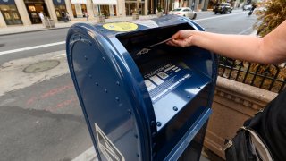 A person drops a letter into a USPS mailbox