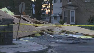 Piles of what appear to be plywood and other debris fills a side street, cordoned off by yellow tape.