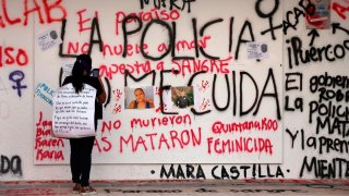 Una ujer toma una fotografía a un mural sobre feminicidios