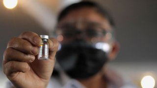 Hombre con cubrebocas negra muestra ampolleta de la vacuna Sinovac