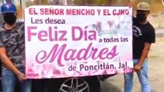 Dos hombres con el rostro cubierto sostienen una manta en el que el Cártel Jalisco supuestamente felicita a las madres