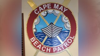 The Cape May Beach Patrol logo depicts a circle with a boat sailing through the ocean. A red band with the words "Cape May Beach Patrol" is seen around the circle.