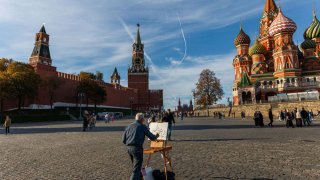 Un artista pinta una vista de la torre Spasskaya del Kremlin y la catedral de San Basilio en un soleado día en Moscú.