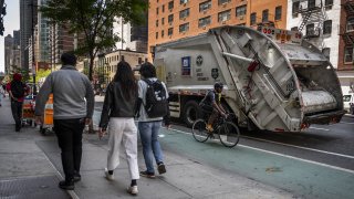 New Yorkers walk on the sidewalk near a Department of Sanitation garbage truck