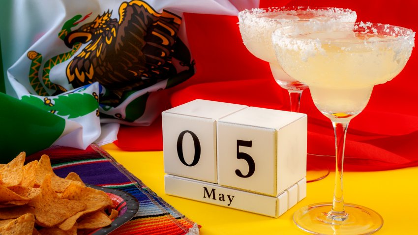 Mexican fiesta and Cinco de Mayo party concept theme with block calendar set on May 5th, traditional rug or serape, two margaritas, bowl of tortilla chips and the flag of mexico