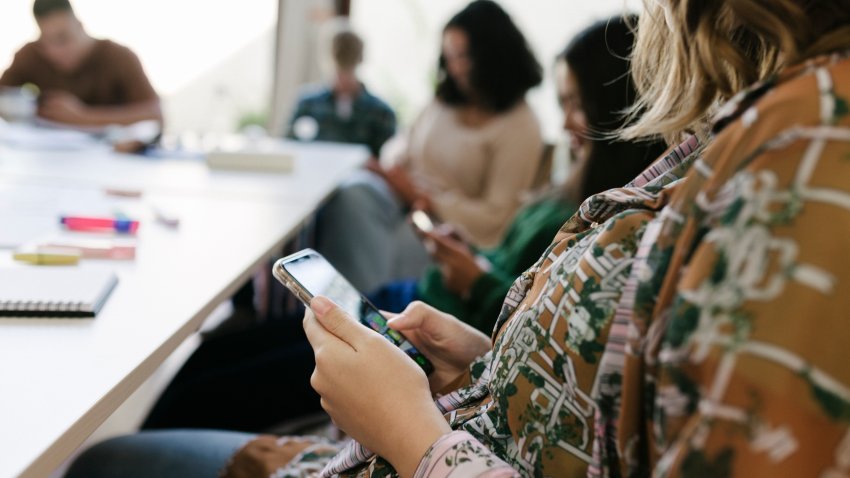 A group of high school students all using their phone at their desks during class while waiting for the lesson to start.