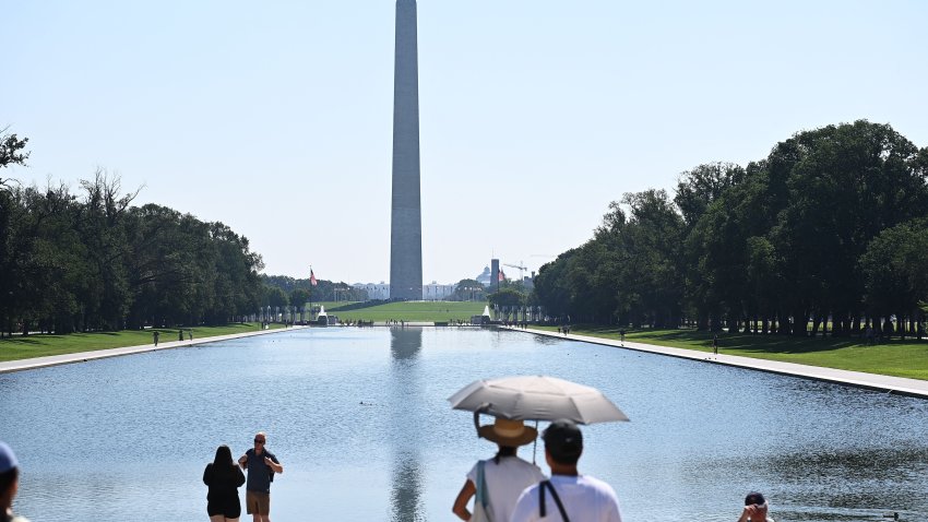 TOPSHOT – People use an umbrella to shelter from the Sun while looking at the Washington Memorial in Washington, DC, on July 23, 2022. – The heat wave blanketing the region is expect to peak this weekend with temperatures near 38C (100F.) (Photo by MANDEL NGAN / AFP) (Photo by MANDEL NGAN/AFP via Getty Images)