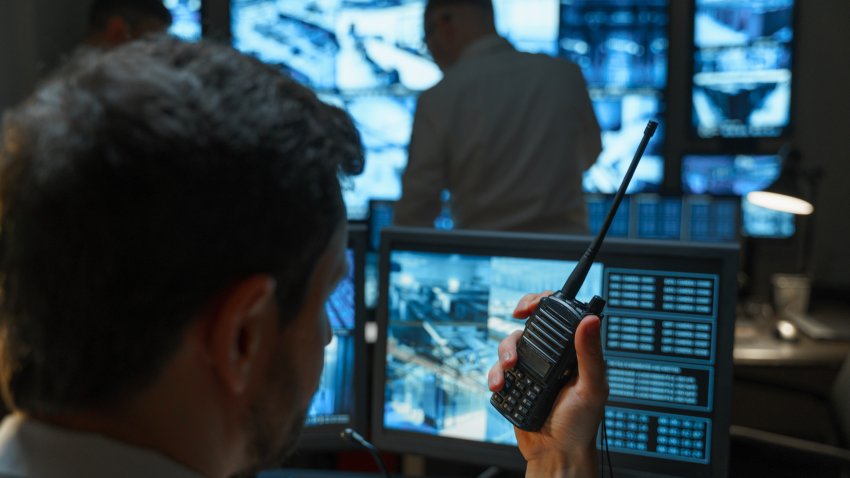 A male security guard in the security room keeps order with the help of modern technologies. The security service monitors display all the information from the surveillance cameras.