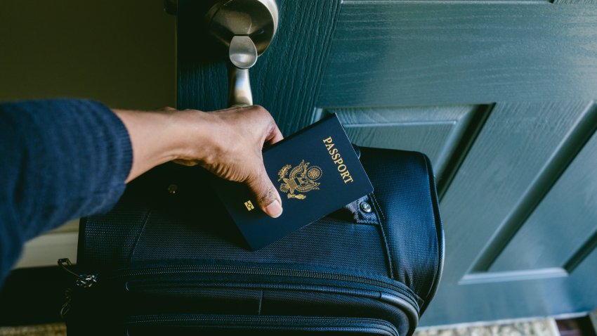 Primer plano de una mujer en la puerta principal preparándose para salir de casa con la maleta hecha y el pasaporte.