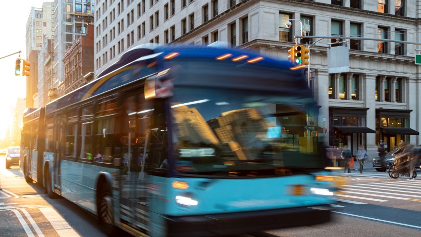 New York City bus driving down 23rd Street through Manhattan with sunlight shining between the buildings in the background