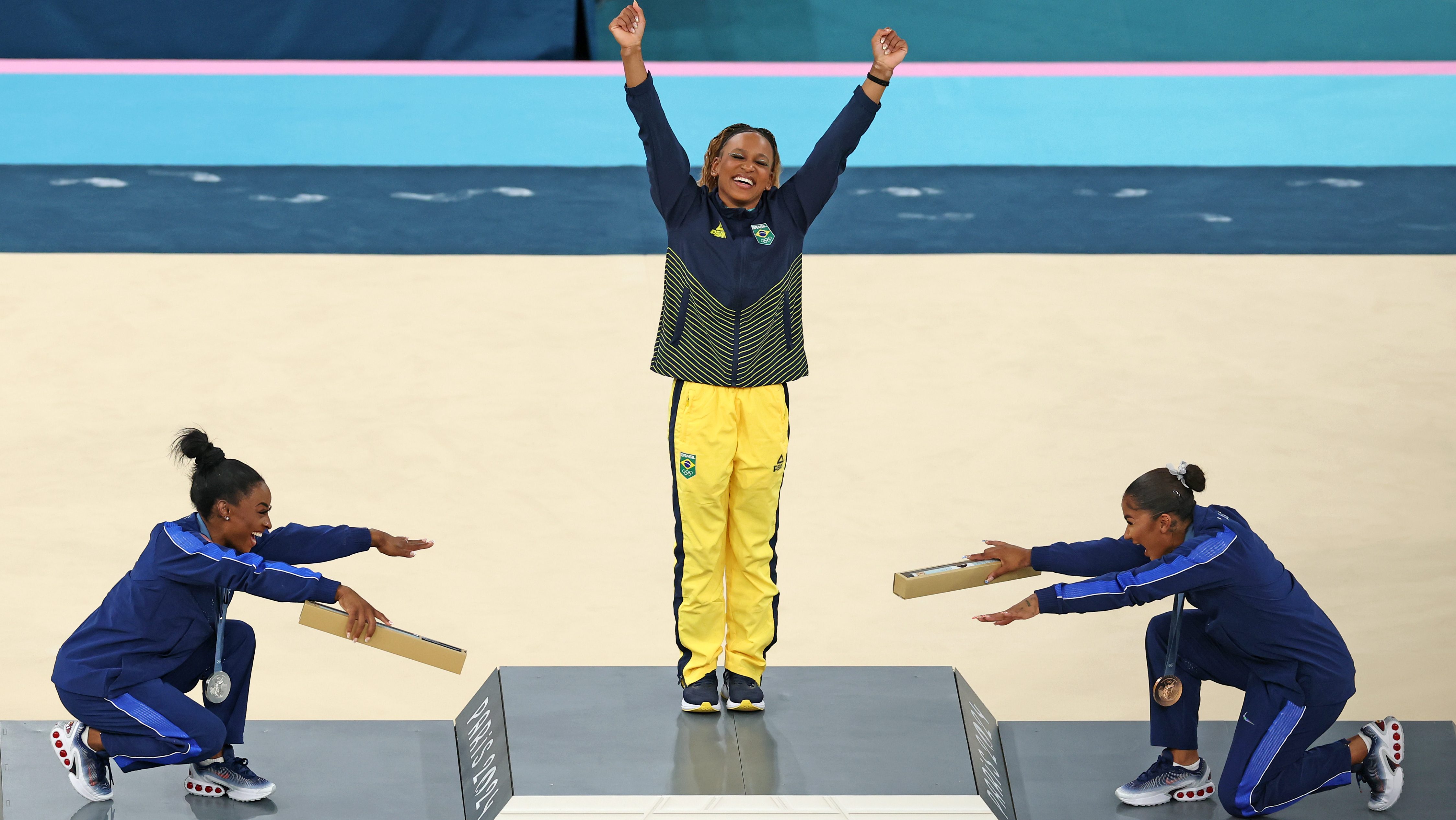 La medallista de oro <a href="https://www.telemundo47.com/deportes/juegos-olimpicos/foto-simone-biles-jordan-chiles-rebeca-andrade-juegos-olimpicos-paris/2493350/" data-type="link" data-id="https://www.telemundo47.com/deportes/juegos-olimpicos/foto-simone-biles-jordan-chiles-rebeca-andrade-juegos-olimpicos-paris/2493350/">Rebeca Andrade</a> (centro) del equipo de Brasil, la medallista de plata Simone Biles (izqquierda) del equipo de Estados Unidos y la medallista de bronce Jordan Chiles (derecha) del equipo de Estados Unidos celebran en el podio de la ceremonia de entrega de medallas de gimnasia artística femenina en el décimo día de los Juegos Olímpicos de París 2024 en Bercy Arena. Ocurrió el 5 de agosto de 2024 en París, Francia, y la foto se volvió viral por su significado. (Foto de Elsa/Getty Images).