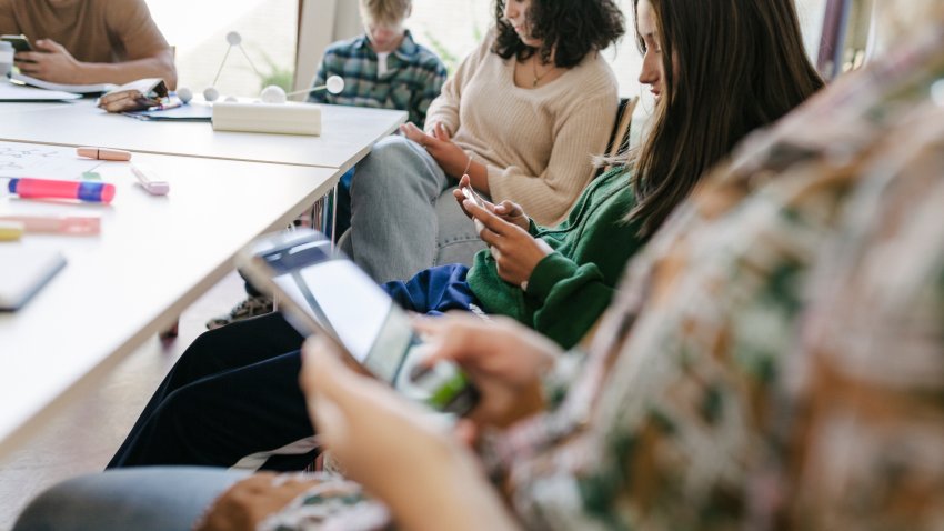 A group of high school students looking at their smartphones while taking a short break during class.