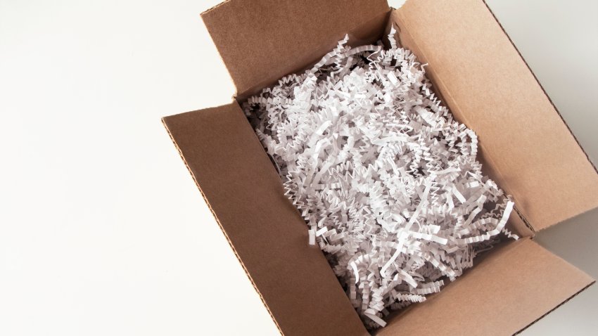 Vertical photo of a cardboard packaging box stuffed with shredded white paper, an ECO-FRIENDLY  solution to packaging since it is biodegradable, a GOOD BUSINESS PRACTICE. Box is on the right hand side and photo is an overhead view of the box.