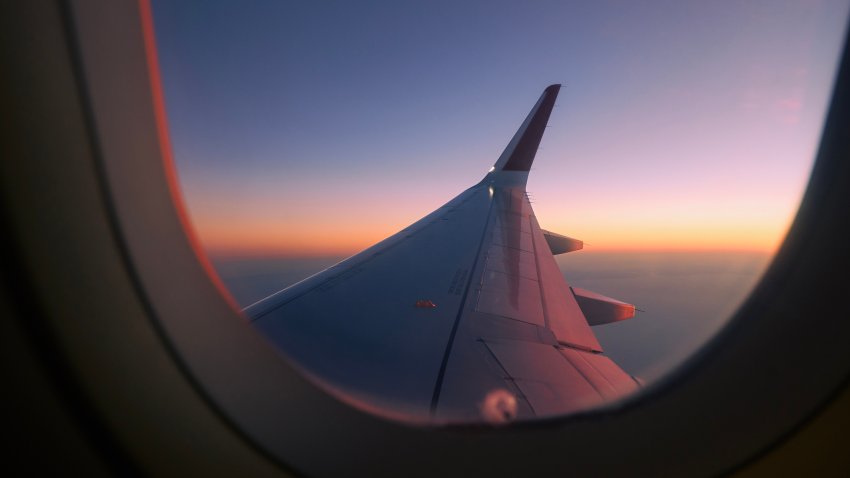 View through airplane window flight above clouds at colorful sunset.