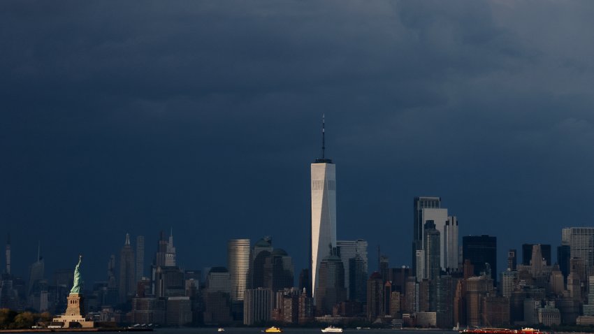 BAYONNE, NJ – MAY 3: The sun sets on the Statue of Liberty and One World Trade Center as storm clouds  behind midtown Manhattan and the Empire State Building in New York City on May 3, 2025, as seen from Bayonne, New Jersey.
