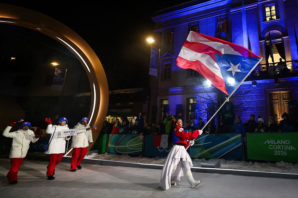 La abanderada de Puerto Rico, Kellie Delka (derecha), desfila junto a otros miembros de la delegación durante la ceremonia de inauguración de los Juegos Olímpicos de Invierno de Milano Cortina 2026 en Cortina d'Ampezzo, en el norte de Italia, el 6 de febrero de 2026. (Foto de Franck FIFE / AFP a través de Getty Images)