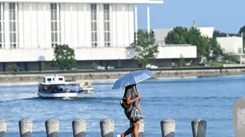 A person uses an umbrella to stay cool while walking along the Potomac River during a heatwave in Washington, DC, on July 1, 2026. Tens of millions of Americans sweltered under furnace-like temperatures this week as central and eastern cities hunkered down for a heat wave set to last through the July 4 holiday weekend. Dozens of local temperature records could be broken, the National Weather Service (NWS) warned, with temperatures in many places to surpass 100 degrees Fahrenheit (38 degrees Celsius) and high humidity pushing the heat index as high as 115 degrees. (Photo by Alex WROBLEWSKI / AFP via Getty Images)