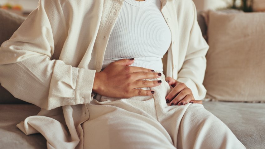Woman, hands and stomach pain of menstruation on sofa with period cramps, bloating or pms in home. Person, abdomen and endometriosis with constipation, nausea and digestion problem on couch in lounge